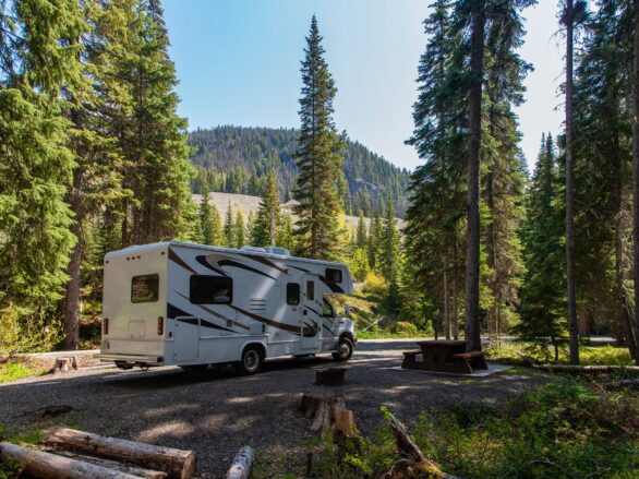 Beautiful campsite in the mountains with an RV and wooden bench.