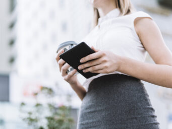 low-angle-view-businesswoman-holding-smartphone-disposable-coffee-cup-outdoors